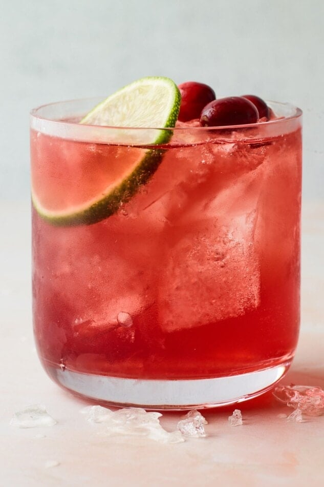 A closeup photo of a short glass filled with vodka cranberry over ice and topped with a slice of lime and a few whole cranberries.