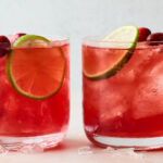 Two glasses filled with vodka cranberry over ice. Each has been topped with a slice of lime and a few whole cranberries.