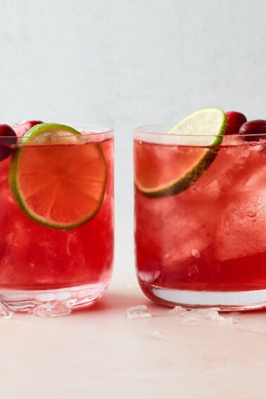 Two glasses filled with vodka cranberry over ice. Each has been topped with a slice of lime and a few whole cranberries.