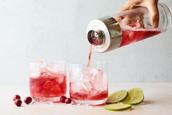 Two glasses. One glass containing vodka cranberry, the other glass being filled with vodka cranberry from a shaker above.