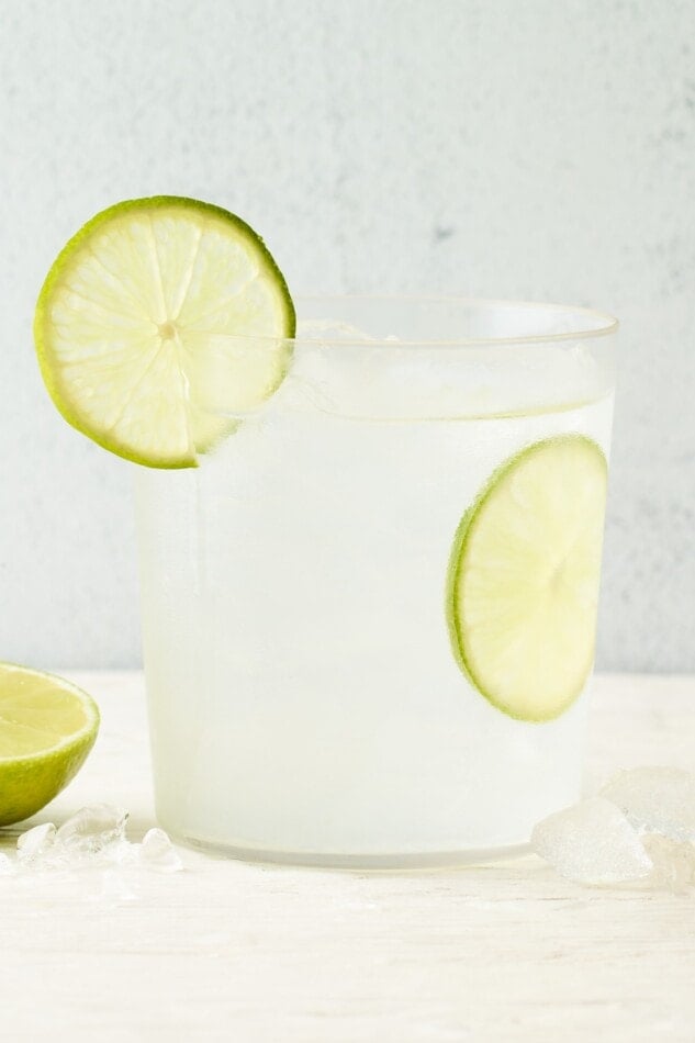 A drink glass containing vodka soda. A slice of lime is in the glass and another on the rim.