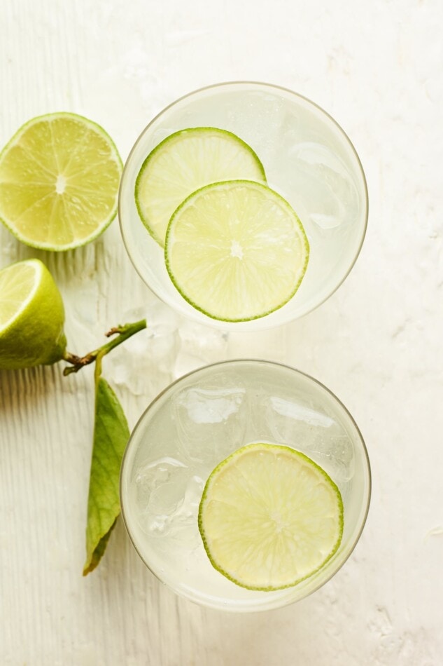 An overhead view of two drink glasses containing vodka soda. Each glass has lime slices resting on top.