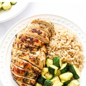 An overhead photo of a plate containing a sliced air fryer chicken breast served with brown rice and zucchini.