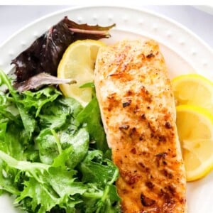 Overhead photo of a plate with filet of air fryer salmon served with leafy greens and lemon slices.