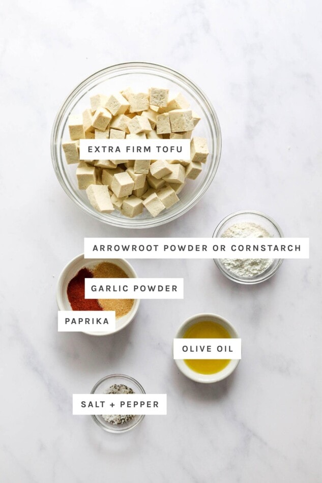 Ingredients measured out to make air fryer tofu: tofu cubes, arrowroot powder/cornstarch, garlic powder, paprika, olive oil, salt and pepper.