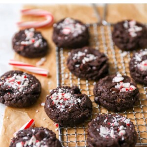 Chocolate peppermint cookies on a wire cooling rack and brown parchment paper. Candy cane pieces are scattered around.