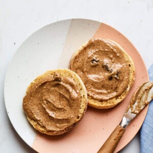 A plate with two halves of an english muffin, slathered with homemade cinnamon raisin almond butter.