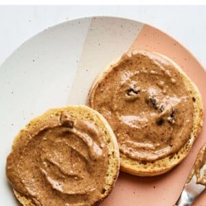 A plate with two halves of an english muffin, slathered with homemade cinnamon raisin almond butter.