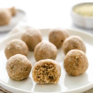 Eight coconut protein balls on a plate, the front and center ball has a bite taken out of it, exposing the inside.