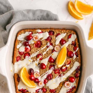 An overhead photo of a baking dish with cranberry orange baked oatmeal topped with a maple orange glaze, orange slices and whole cranberries.