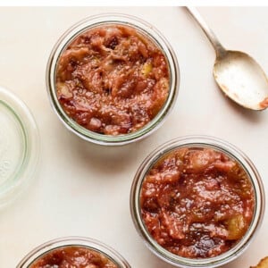 An overhead photo looking down at 3 jars of homemade fig jam. A spoon and two slices of toasted bread are next to the jars.