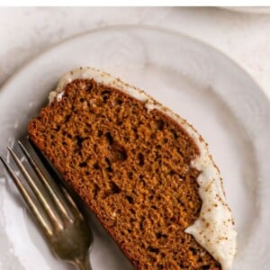 A slice of gingerbread loaf with maple cream cheese frosting on a plate. A fork rests on the plate next to the slice.