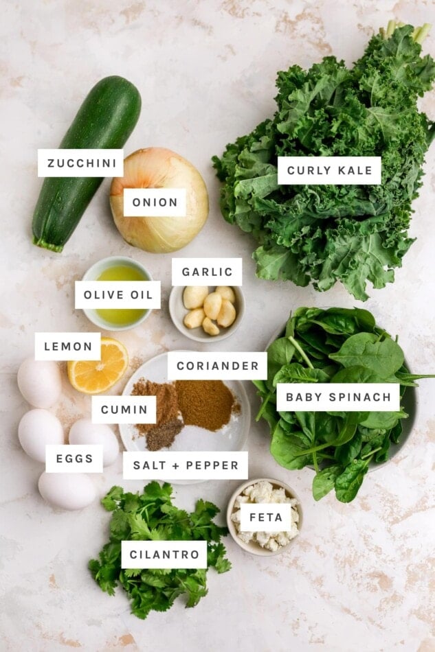 Ingredients measured out to make greek shakshuka: zucchini, onion, curly kale, garlic, olive oil, lemon, coriander, baby spinach, cumin, eggs, salt, pepper, feta and cilantro.