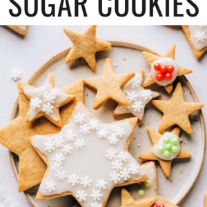 An overhead photo looking at a plate of healthy sugar cookies. Some of the cookies have been decorated with white icing and red, green or white sprinkles and some of the cookies are plain.