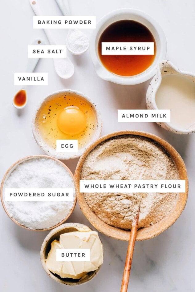 Ingredients measured out to make healthy sugar cookies: baking powder, maple syrup, sea salt, vanilla, almond milk, egg, whole wheat pastry flour, powdered sugar and butter.