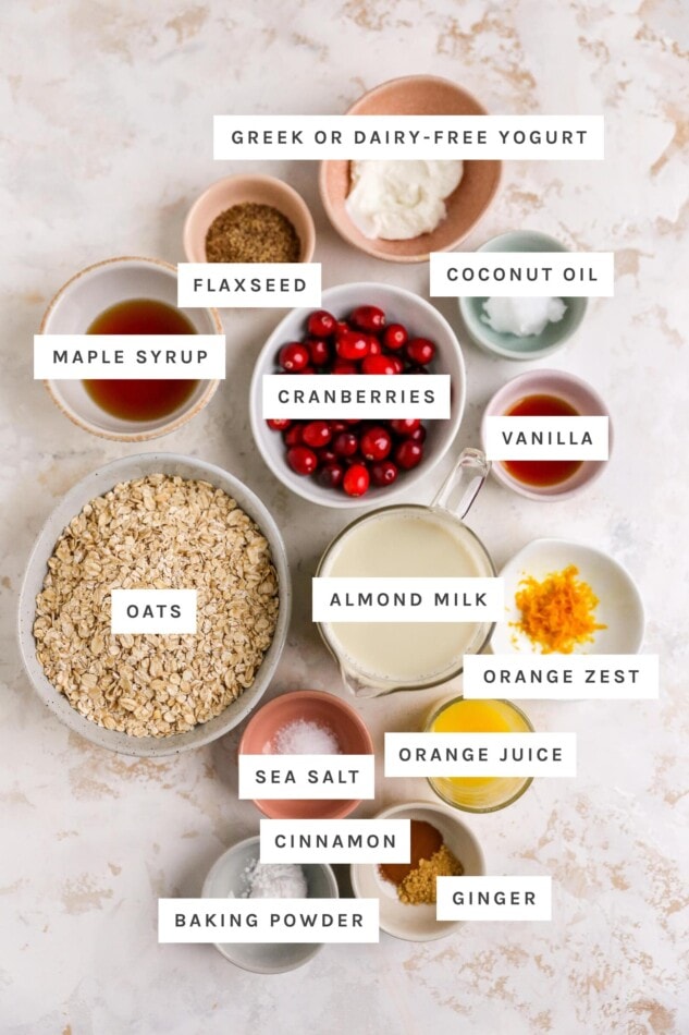 Ingredients measured out to make cranberry orange baked oatmeal: greek yogurt, coconut oil, flaxseed, maple syrup, cranberries, vanilla, oats, almond mik, orange zest, sea salt, orange juice, baking powder, cinnamon and ginger.