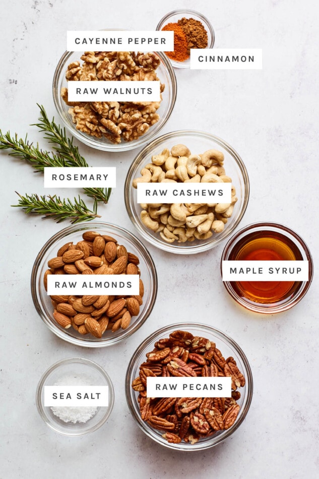 Ingredients measured out to make party nuts: cayenne pepper, cinnamon, raw walnuts, rosemary, raw cashews, raw almonds, maple syrup, sea salt and raw pecans.