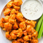 An overhead photo looking at a plate with air fryer buffalo cauliflower, celery sticks and a bowl of ranch for dipping.