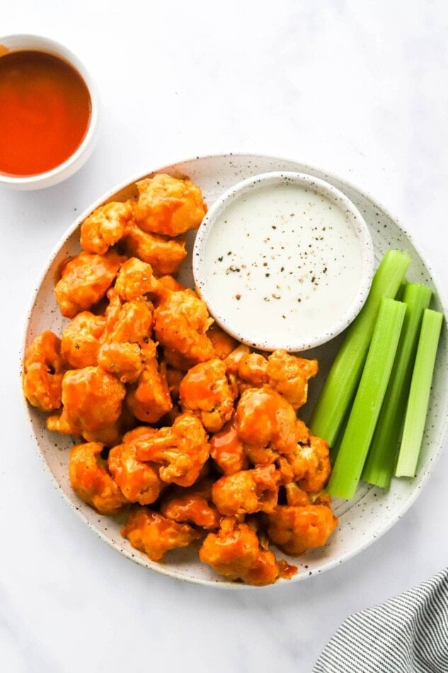 An overhead photo looking at a plate with air fryer buffalo cauliflower, celery sticks and a bowl of ranch for dipping.