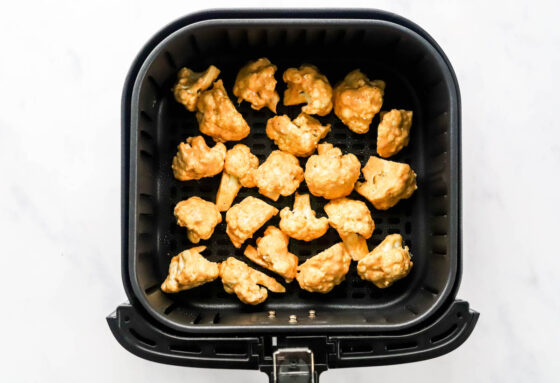 Seasoned cauliflower florets in a air fryer basket.