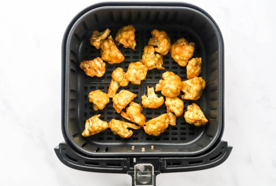 Seasoned cauliflower florets in an air fryer basket after being air fried.