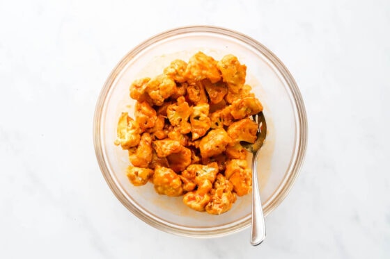 Seasoned and air fried cauliflower florets tossed in buffalo sauce in a mixing bowl.