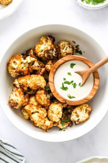An overhead photo looking down at a bowl of air fryer cauliflower. There is a small wooden bowl inside the larger bowl containing ranch dipping sauce.