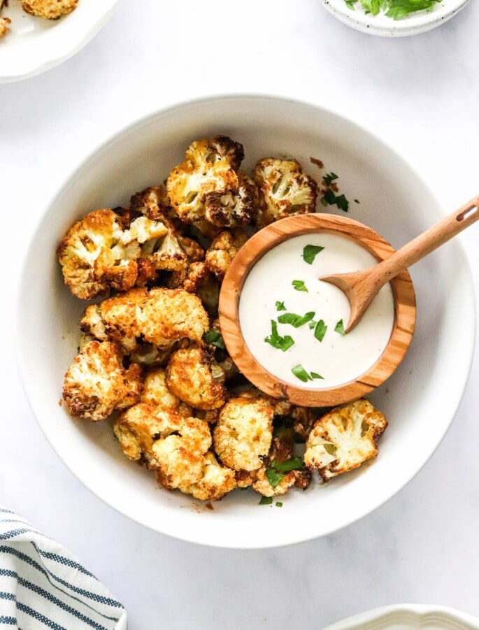 An overhead photo looking down at a bowl of air fryer cauliflower. There is a small wooden bowl inside the larger bowl containing ranch dipping sauce.