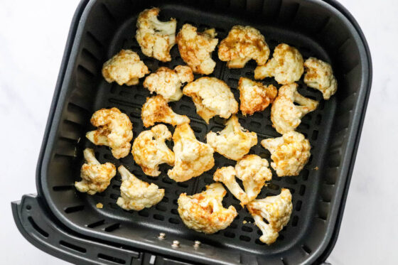 An air fryer basket containing seasoned cauliflower.