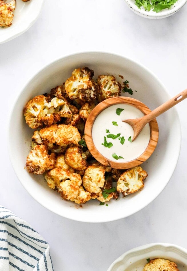 An overhead photo looking down at a bowl containing air fried cauliflower. There is a smaller bowl resting inside the larger bowl with some ranch dip.