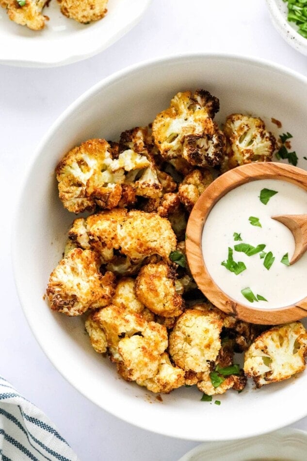 An overhead photo looking down at a bowl containing air fried cauliflower. There is a smaller bowl resting inside the larger bowl with some ranch dip.