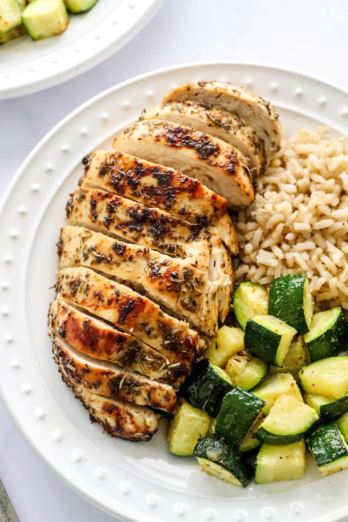 A closeup photo of an air fryer chicken breast sliced and served on a plate with brown rice and zucchini.