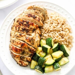 An overhead photo of a plate containing a sliced air fryer chicken breast served with brown rice and zucchini.