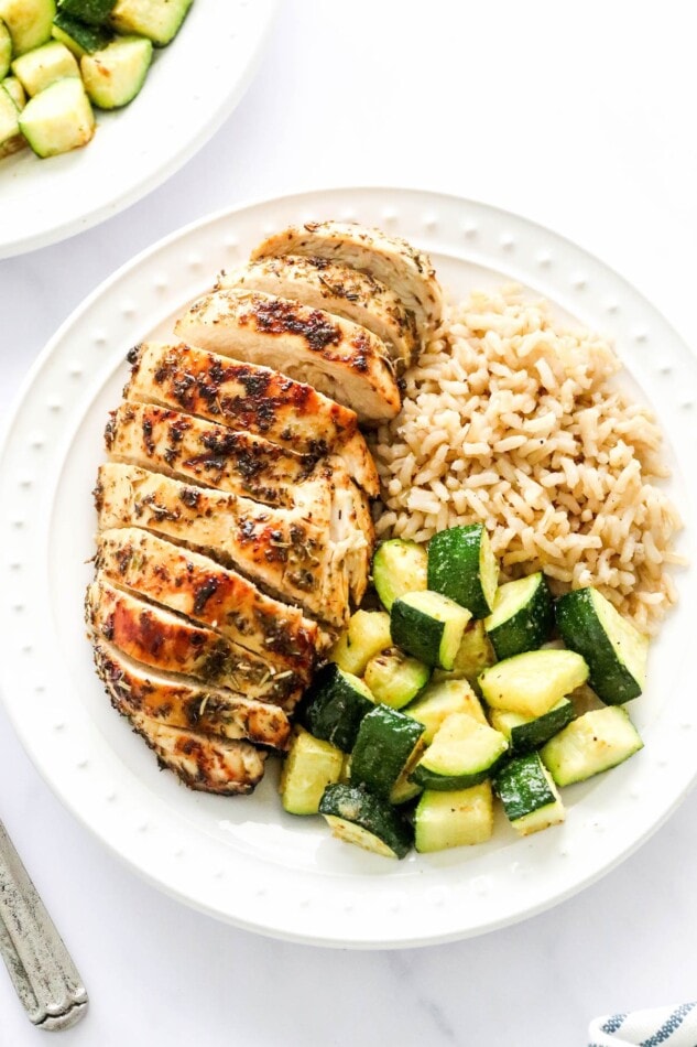 An overhead photo of a plate containing a sliced air fryer chicken breast served with brown rice and zucchini.