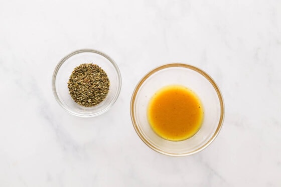 Two small mixing bowls side by side. One contains seasoning and spices. The other contains oil, apple cider vinegar and dijon mustard.