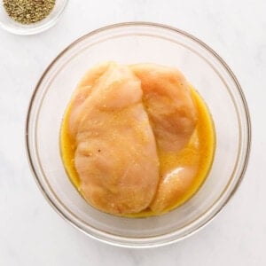 Two chicken breasts in a bowl of oil, apple cider vinegar and dijon mustard.