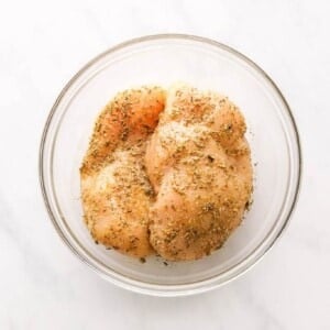 A mixing bowl containing two chicken breasts covered in seasoning.