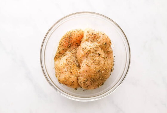 A mixing bowl containing two chicken breasts covered in seasoning.