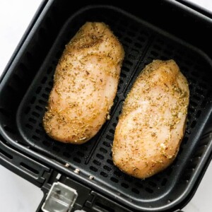 Two seasoned chicken breasts in an air fryer basket.