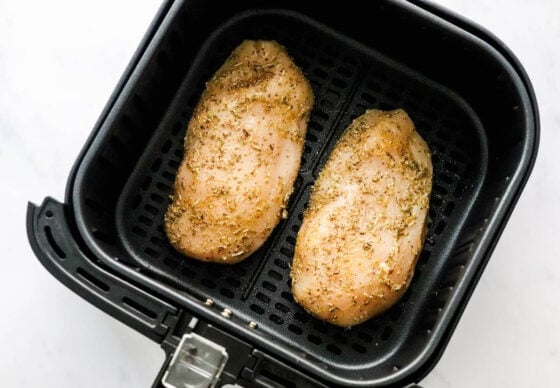 Two seasoned chicken breasts in an air fryer basket.