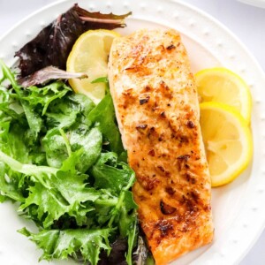 Overhead photo of a plate with filet of air fryer salmon served with leafy greens and lemon slices.