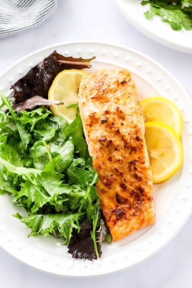 Overhead photo of a plate with filet of air fryer salmon served with leafy greens and lemon slices.