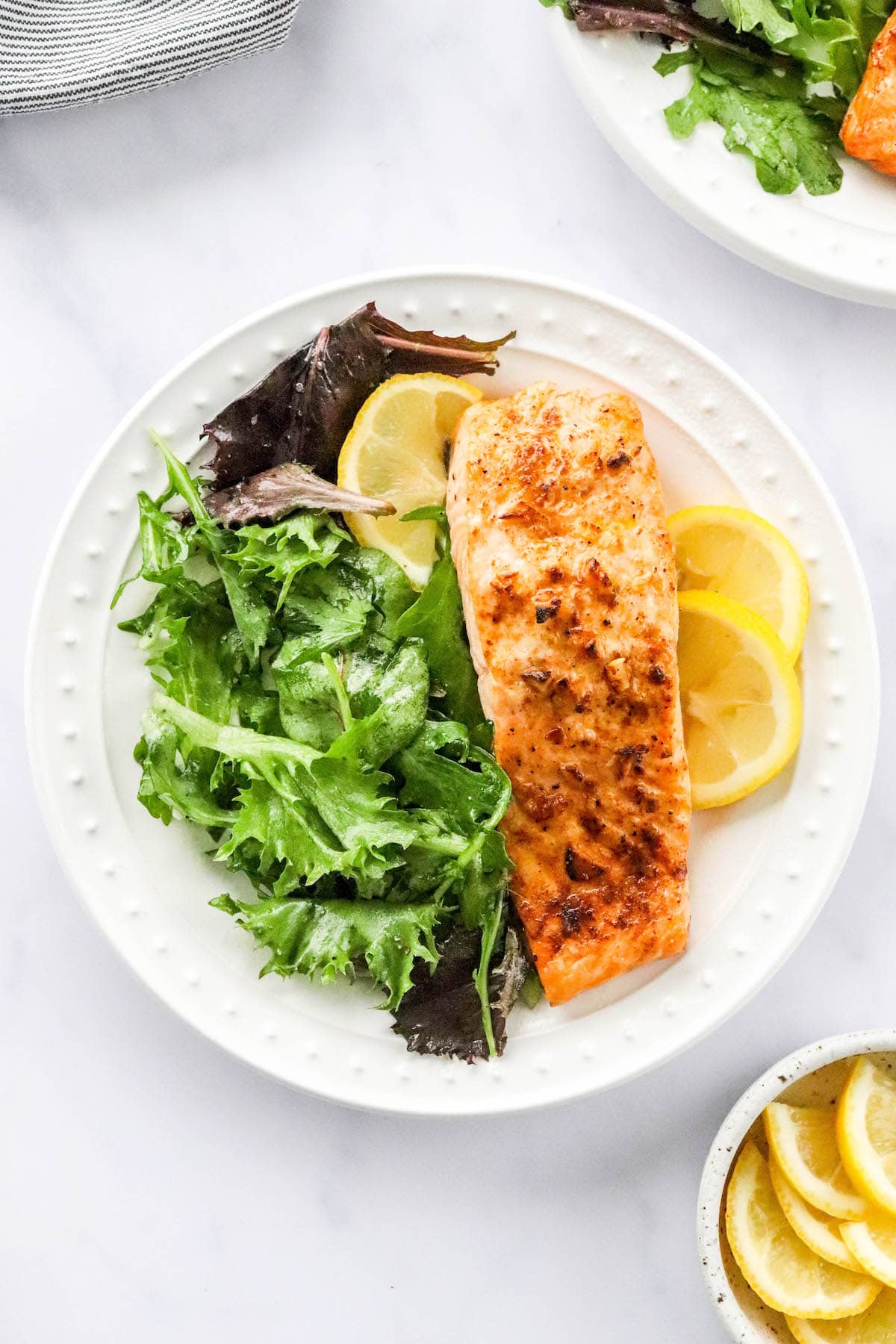 Overhead photo of a plate with filet of air fryer salmon served with leafy greens and lemon slices.