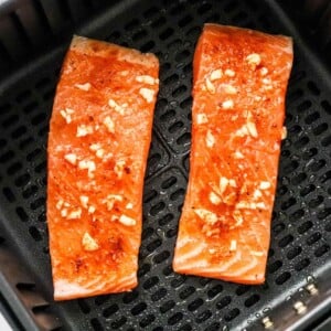 Two seasoned salmon filets in an air fryer basket.