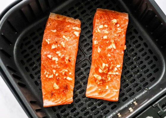 Two seasoned salmon filets in an air fryer basket.