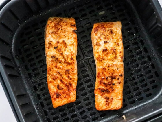 Two air fried filets of salmon in an air fryer basket.