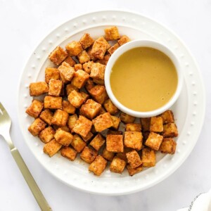 An overhead photo of a plate of air fried tofu with a ramekin of dipping sauce. A gold fork is next to the plate.