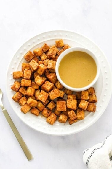 An overhead photo of a plate of air fried tofu with a ramekin of dipping sauce. A gold fork is next to the plate.