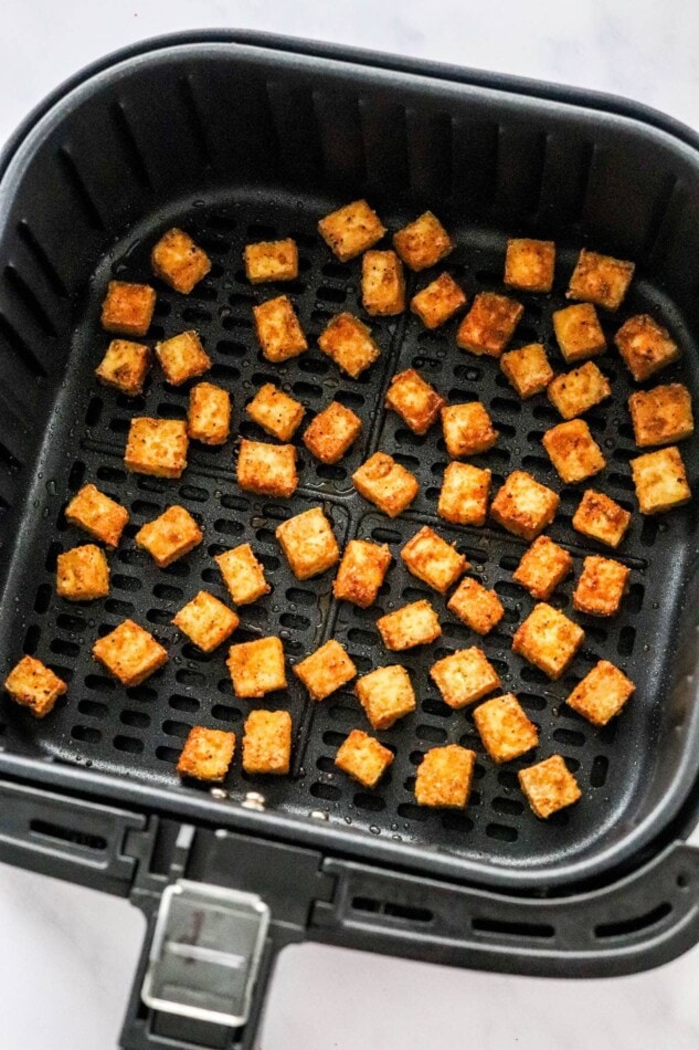 Perfectly air fried tofu in an air fryer basket.