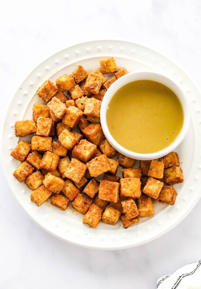 An overhead photo looking down at a plate of air fried tofu. There is a ramekin of dipping sauce on the plate.